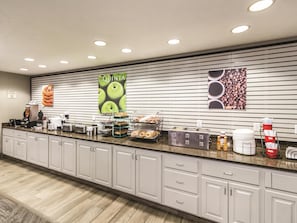 A hotel breakfast area with a counter, coffee machines, and a variety of food items. - La Quinta Inn & Suites by Wyndham Fargo-Medical Center (Fargo)