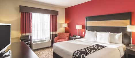 A hotel room with a large bed, a desk, a chair, a TV, and a window with curtains.
