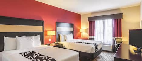 A hotel room with two beds, a desk, a TV, and a window with curtains.