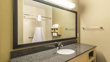 A bathroom with a granite countertop, a sink, a mirror, a towel rack, and a towel dispenser.