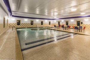 Una piscina interior con diseño de pared a cuadros, una zona de estar con mesas y sillas, y un suelo de baldosas.