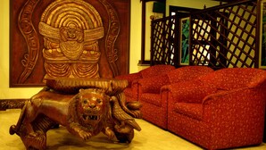 A room with a lion sculpture, a red patterned sofa, and a decorative wooden panel. - Eastend Munnar (Devikolam)