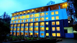 A multi-story hotel with balconies and a well-lit facade. - Eastend Munnar (Devikolam)