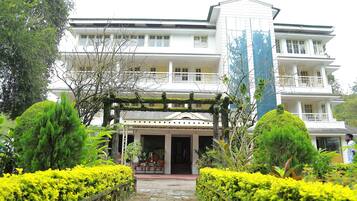 A multi-story hotel with a central entrance, surrounded by well-maintained gardens and a clear pathway leading to the entrance.