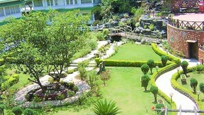 A well-maintained garden with a central lawn, surrounded by neatly trimmed hedges and various trees. - Eastend Munnar (Devikolam)