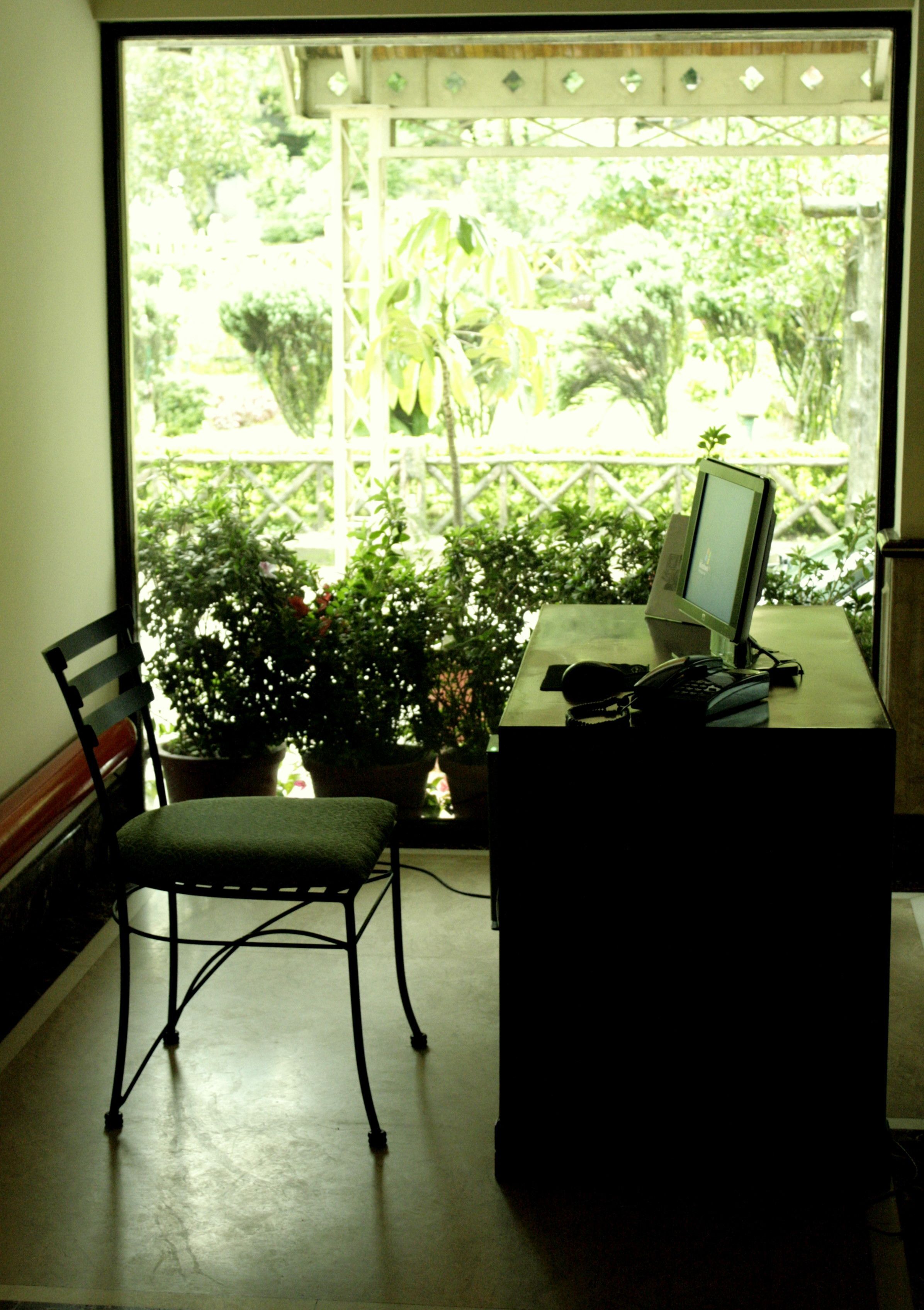 Una habitación con escritorio, silla y ventana con vistas a un jardín.
