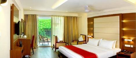 A hotel room with a large bed, a desk, a chair, a TV, and a balcony with curtains.