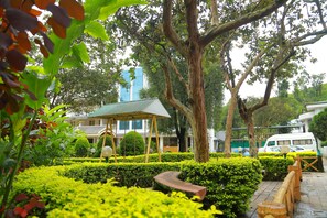 Un jardín bien cuidado con un pabellón, setos recortados y un árbol grande.