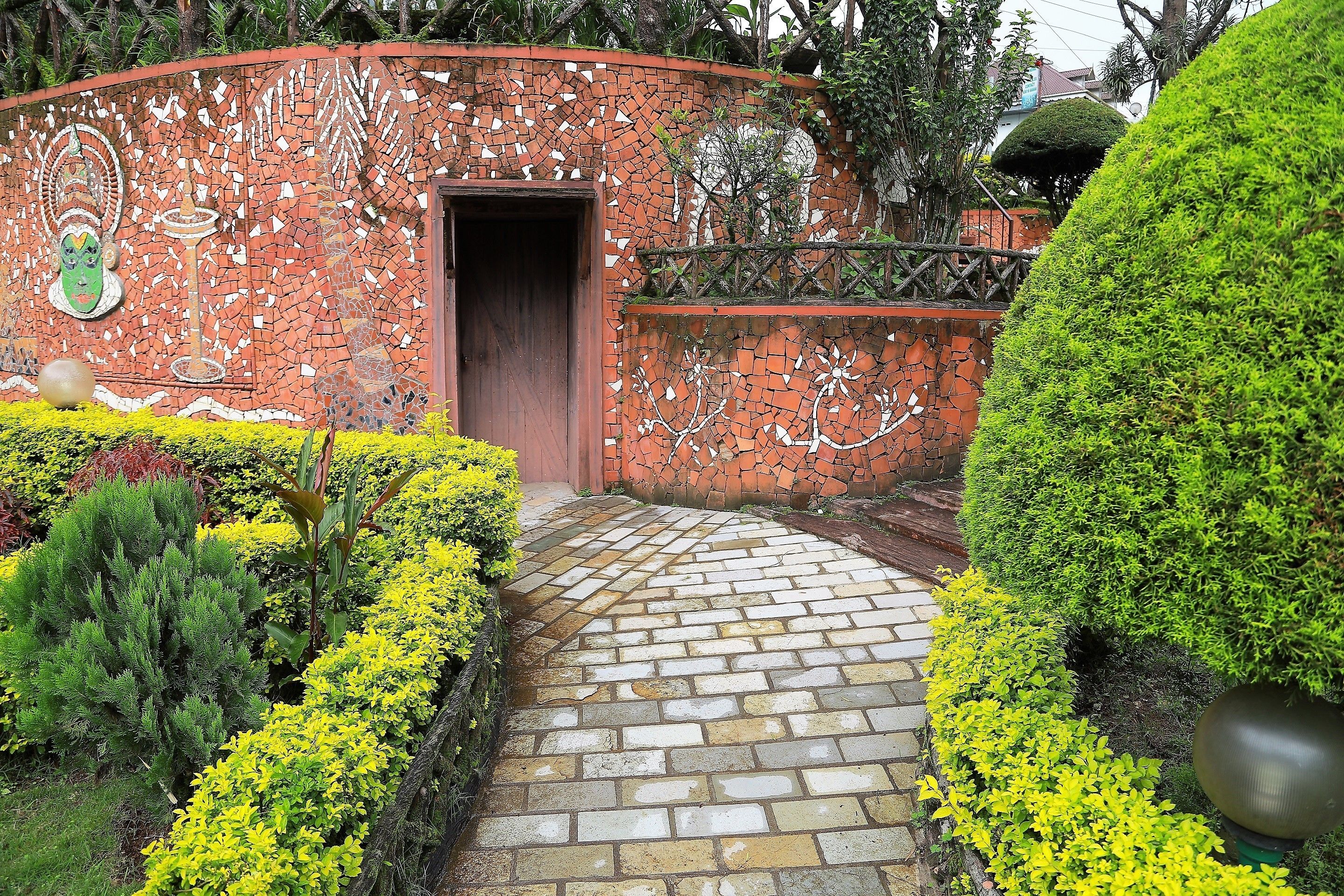 A brick pathway leading to a door, surrounded by neatly trimmed hedges and plants.