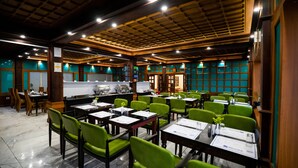 A restaurant with a traditional wooden ceiling, green chairs, and tables set for dining. - Hill View Munnar (Devikolam)