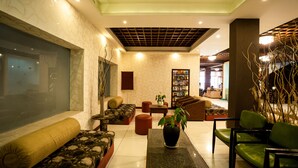 A modern lobby with a sofa, chairs, a coffee table, and a bookshelf. - Hill View Munnar (Devikolam)