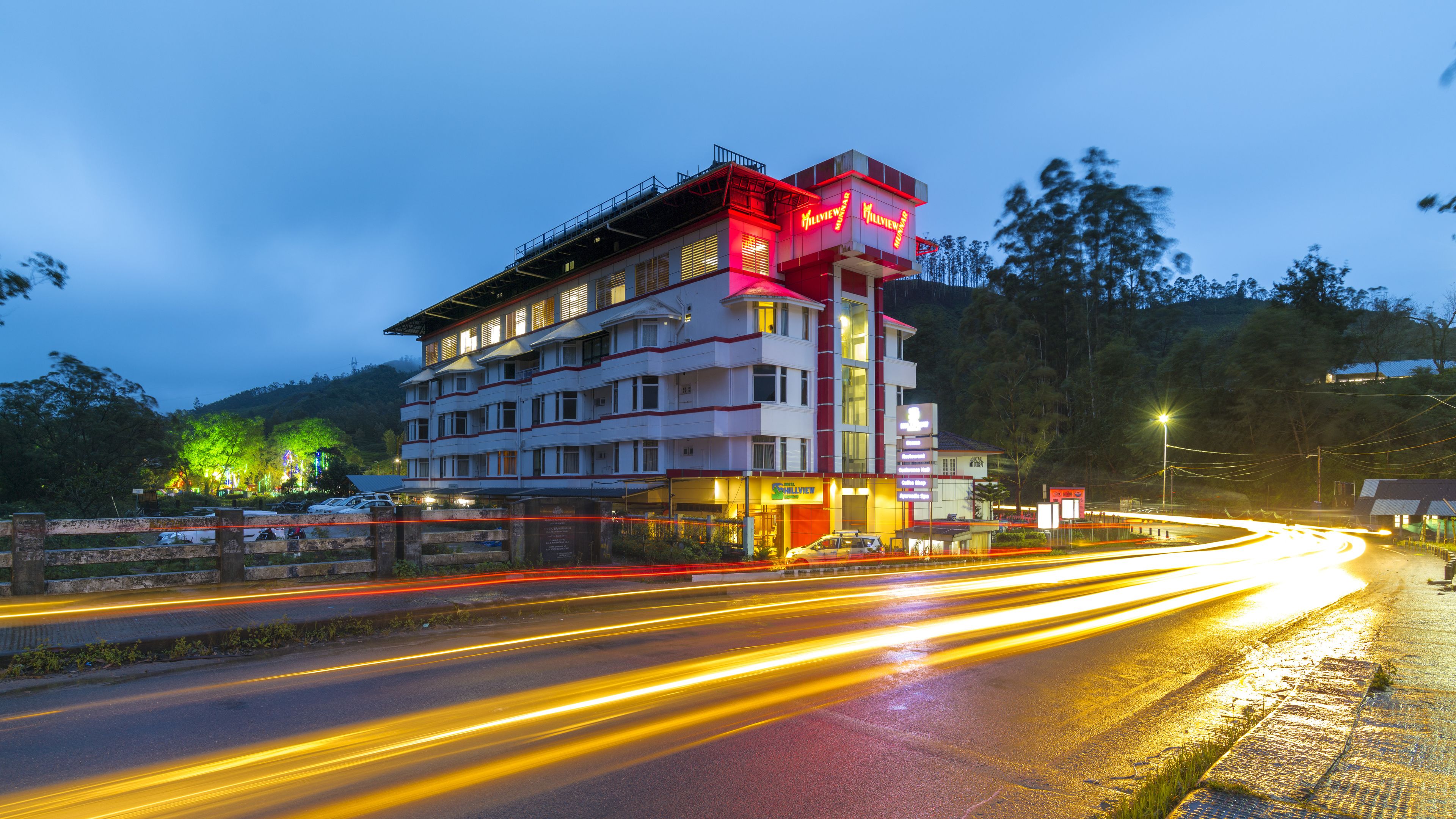 A multi-story hotel with a prominent red and white facade, multiple balconies, and a well-lit entrance.