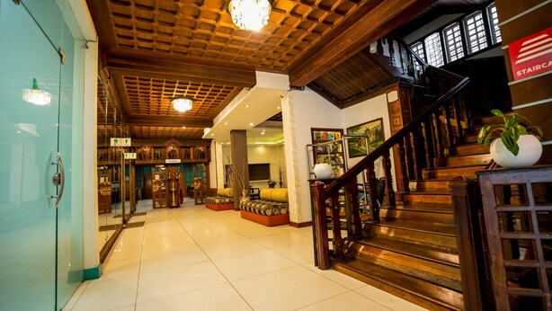 A hotel lobby with a wooden staircase, a reception desk, and a dining area. - Hill View Munnar (Devikolam)