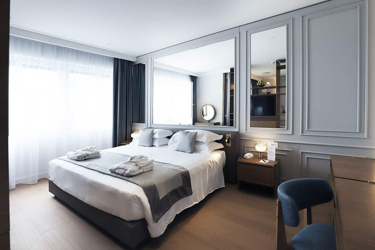 Een moderne hotelkamer met een groot bed, nachtkastjes, een spiegel en een stoel.