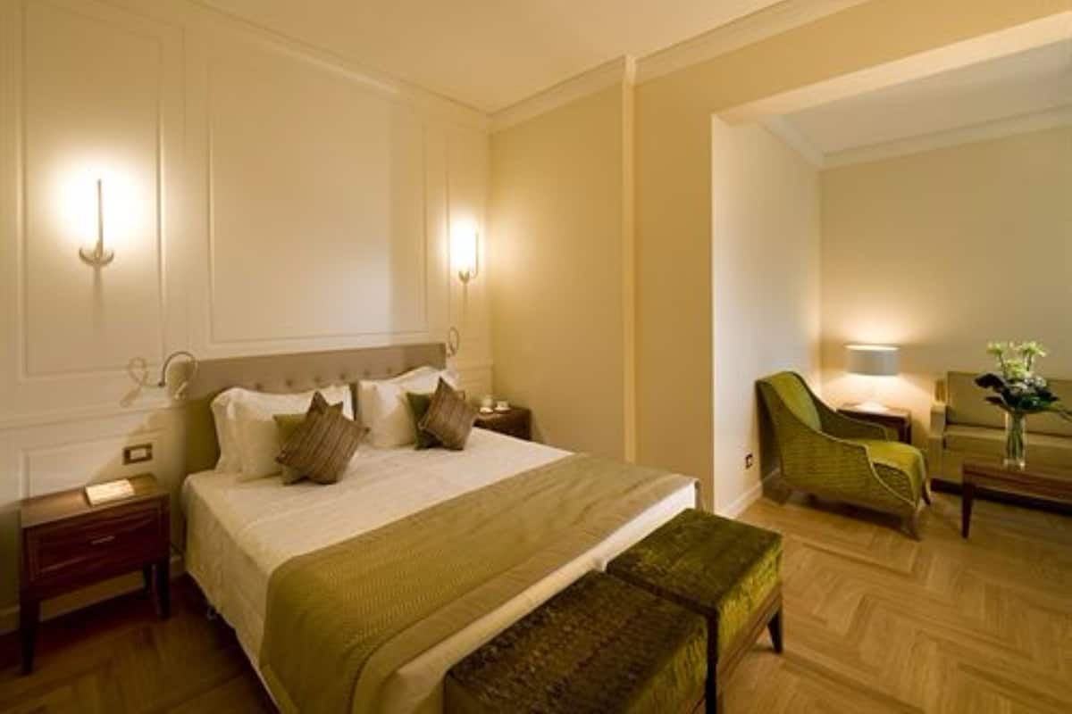 Een hotelkamer met een groot bed, nachtkastjes, een bankje en een stoel.