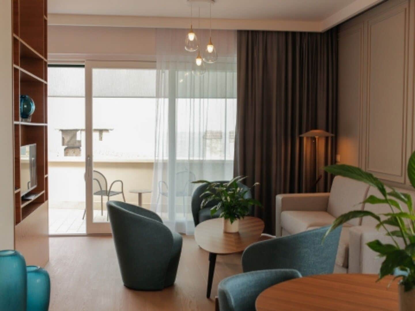 A modern living room with a sofa, chairs, a coffee table, and a potted plant. There is a sliding glass door leading to an outdoor area.