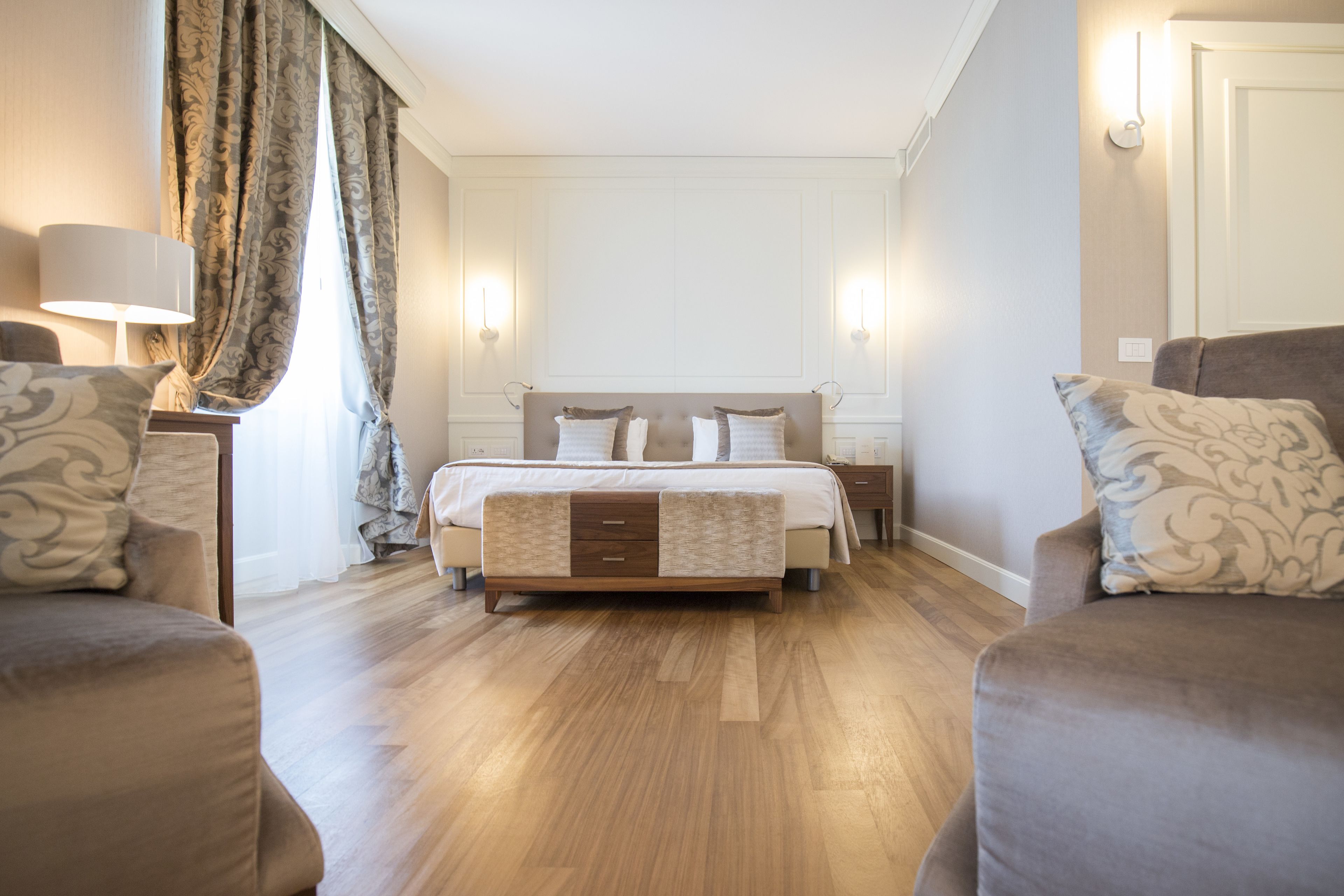 A hotel room with a large bed, two bedside tables, a nightstand, and a sofa.