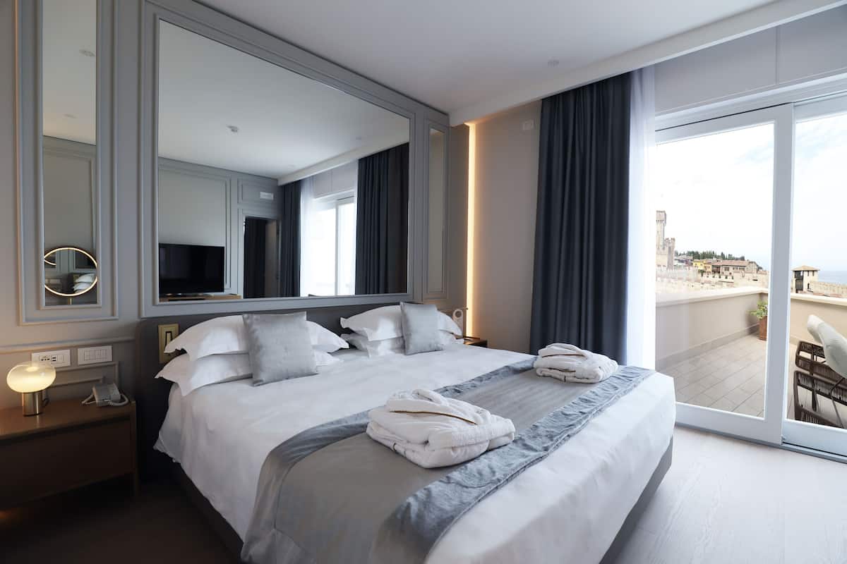 Hotelkamer met een groot bed, een flatscreen televisie, een nachtkastje met lamp en uitzicht op de stad door een groot raam.