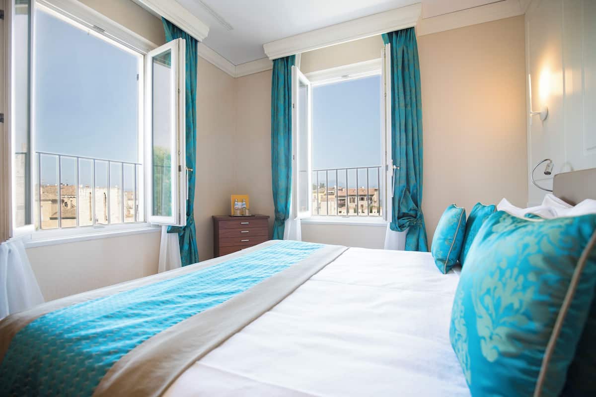 Een hotelkamer met een bed, een nachtkastje, een raam met gordijnen en uitzicht op gebouwen.