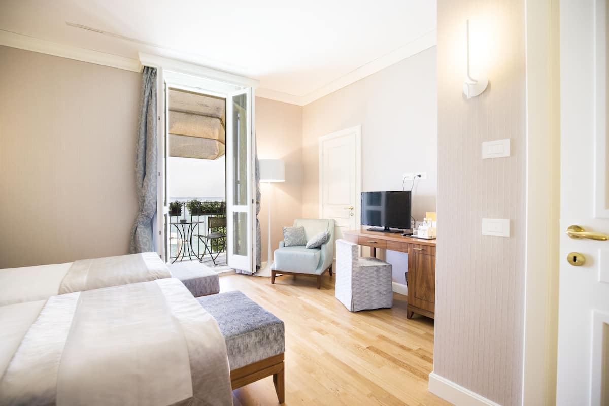 Een hotelkamer met twee bedden, een bureau met een televisie, een stoel en een balkon met een tafel en stoelen.