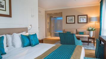 Ein Hotelzimmer mit einem großen Bett, einer Sitzecke mit einer Couch und Sesseln, einem Schreibtisch und einem durch eine geöffnete Tür einsehbaren Badezimmer.