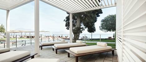 A covered outdoor lounge area with multiple seating options, a view of the sea, and a pergola structure.