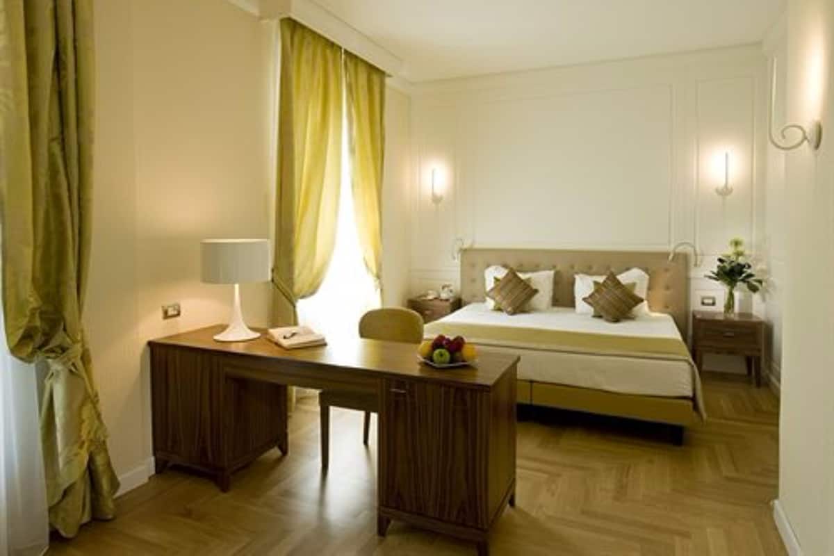 Een hotelkamer met een bed, nachtkastje, lamp en een bureau met stoel.