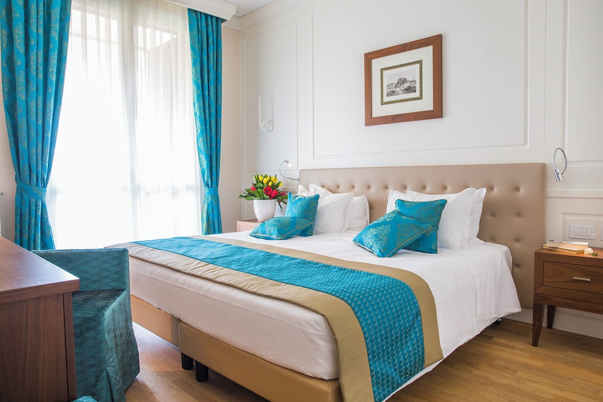 Een hotelkamer met een groot bed, een houten nachtkastje, een bureau en een ingelijste foto aan de muur.