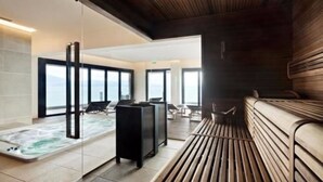 Ein moderner Wellnessbereich mit Whirlpool, Sitzgelegenheiten und großen Fenstern mit Meerblick.