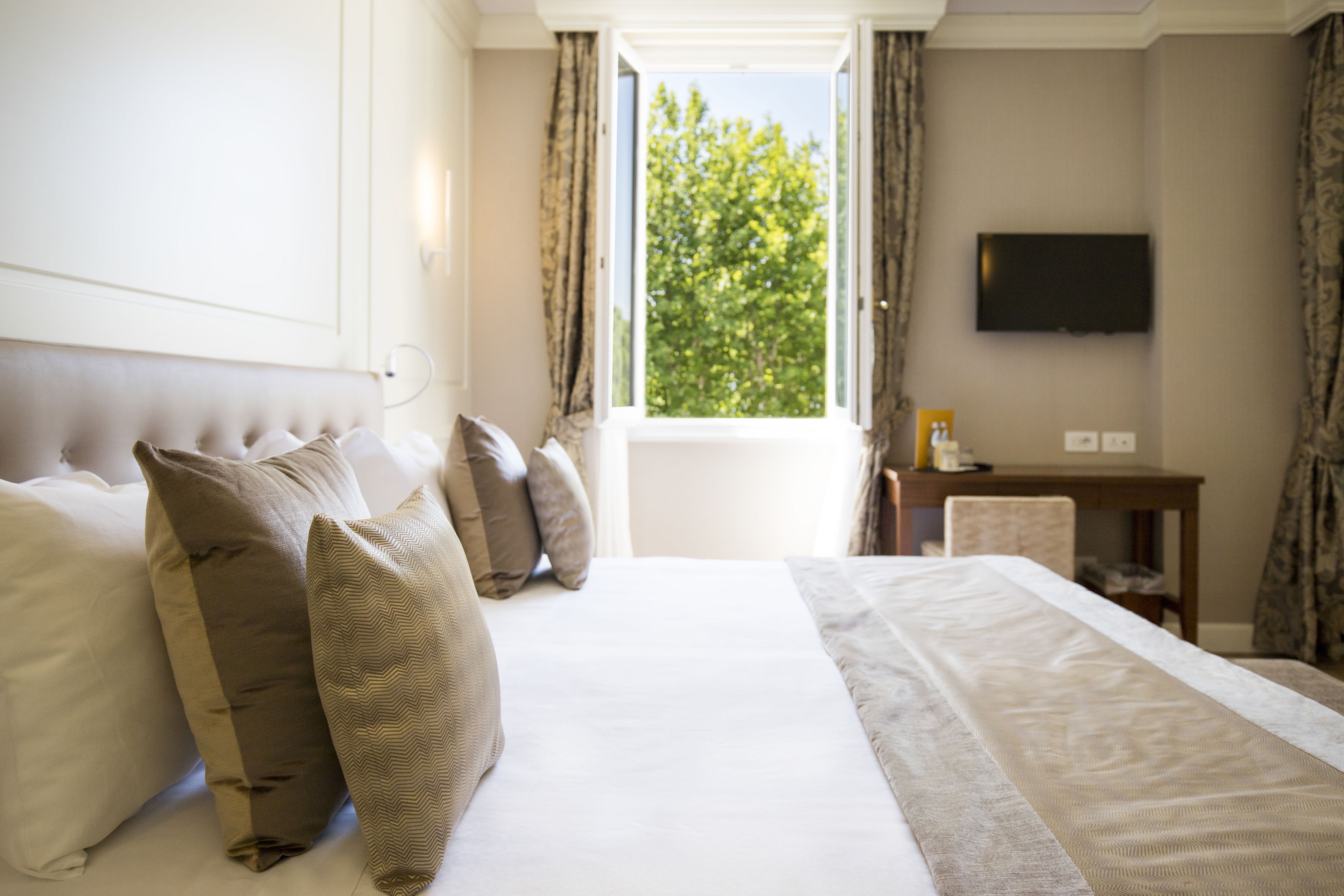 A hotel room with a large bed, a flat-screen TV mounted on the wall, and a window with curtains.