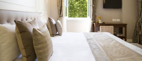 A hotel room with a large bed, a flat-screen TV mounted on the wall, and a window with curtains.