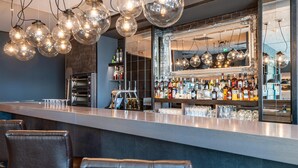 A bar area with a long counter, multiple hanging light fixtures, a large mirror, and a variety of bottles and glasses on shelves. - Premier Inn Nürnberg City Nordost (Nuremberg)