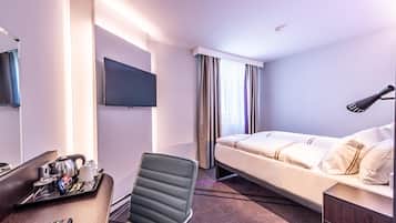 A hotel room with a bed, a desk with a tray of breakfast items, a chair, a TV, and a window with curtains.