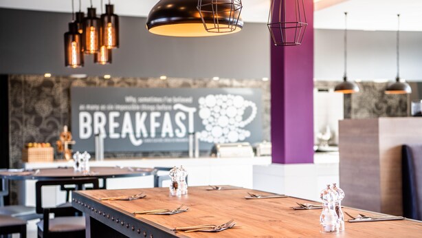 A restaurant interior with wooden tables, metal chairs, pendant lighting, and a sign reading 'BREAKFAST.' - Premier Inn Nürnberg City Nordost (Nuremberg)
