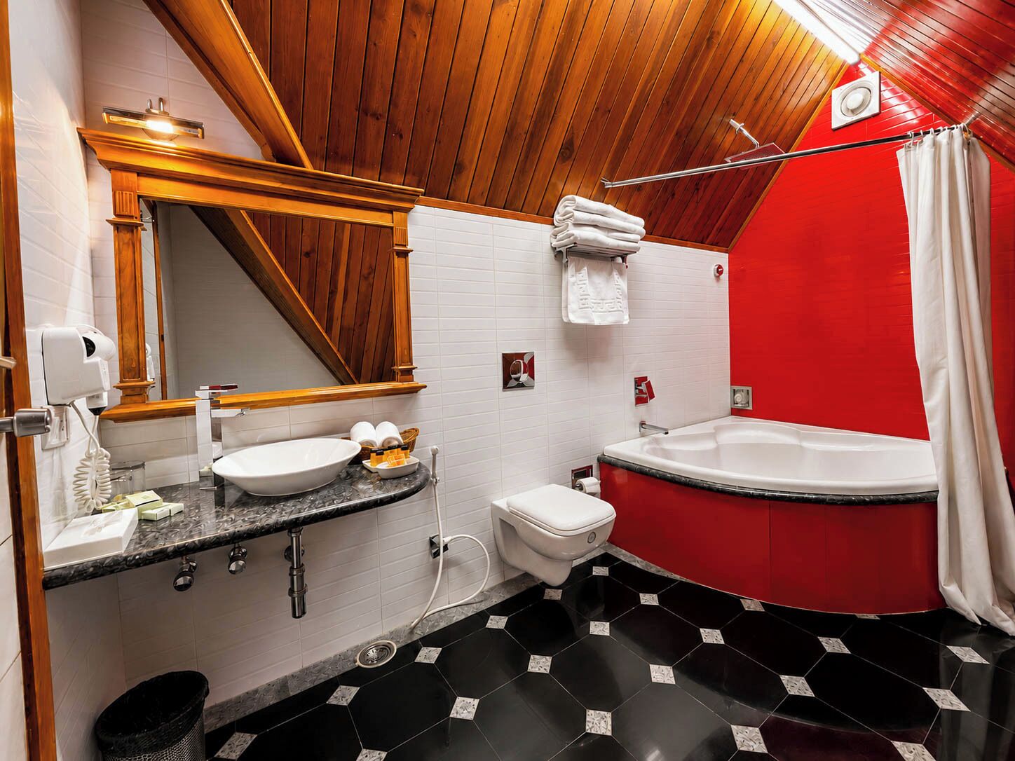 Een badkamer met een houten plafond, een wastafel, een toilet en een rood bad.