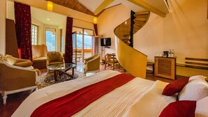 A hotel room with a bed, two armchairs, a small table, a spiral staircase, and a view of the mountains.