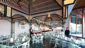 A restaurant with a high ceiling and lattice design, featuring tables with white chairs and a marble floor.