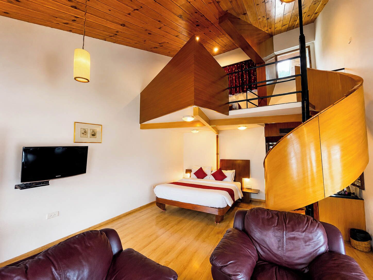 Quarto de hotel moderno com teto de madeira, cama com almofadas vermelhas, televisão e sofá de couro.