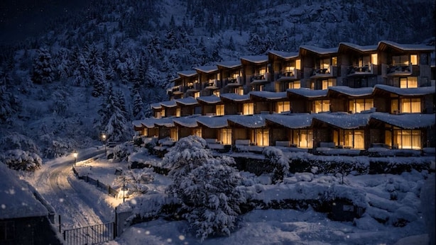 A snow-covered resort with multiple wooden buildings, a winding path, and a mountainous backdrop.