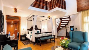Amplia sala de estar con techo alto, escalera de madera, cama con dosel, piano y sillón azul.