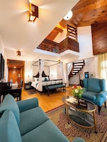 Amplia sala de estar con techo alto, escalera de madera, cama con dosel, piano y sillón azul.