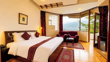 Habitación de hotel con una cama grande, un sofá, una mesita y vistas a la ciudad a través de amplios ventanales.