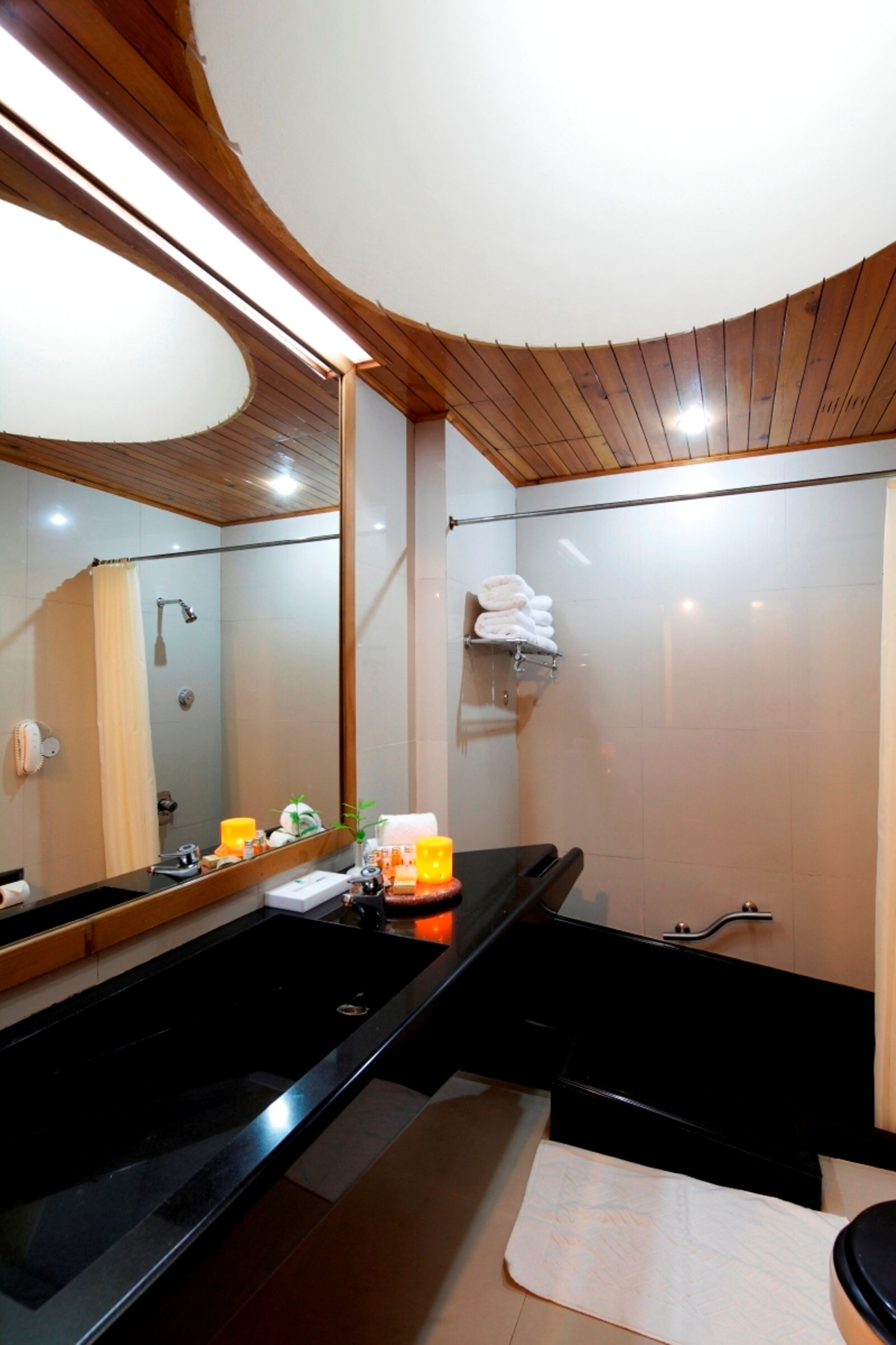 Ein modernes Badezimmer mit einem schwarzen Waschbecken, einem großen Spiegel und einer Holzbalkendecke.