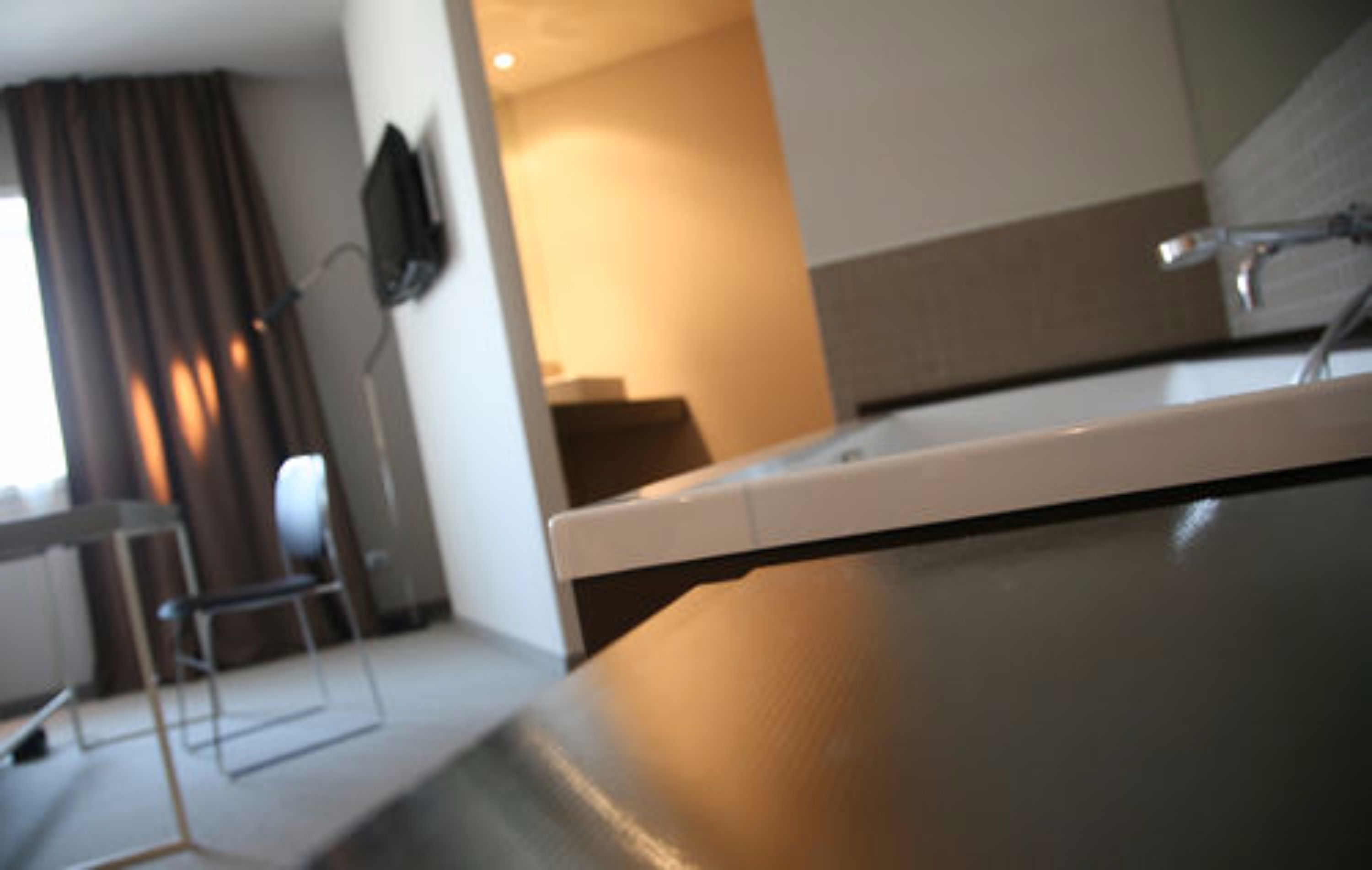 Uma casa de banho moderna com banheira, espelho e televisão montada na parede.