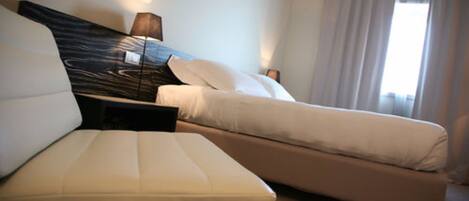Una habitación de hotel con una cama, un sofá, una lámpara y una ventana con cortinas.