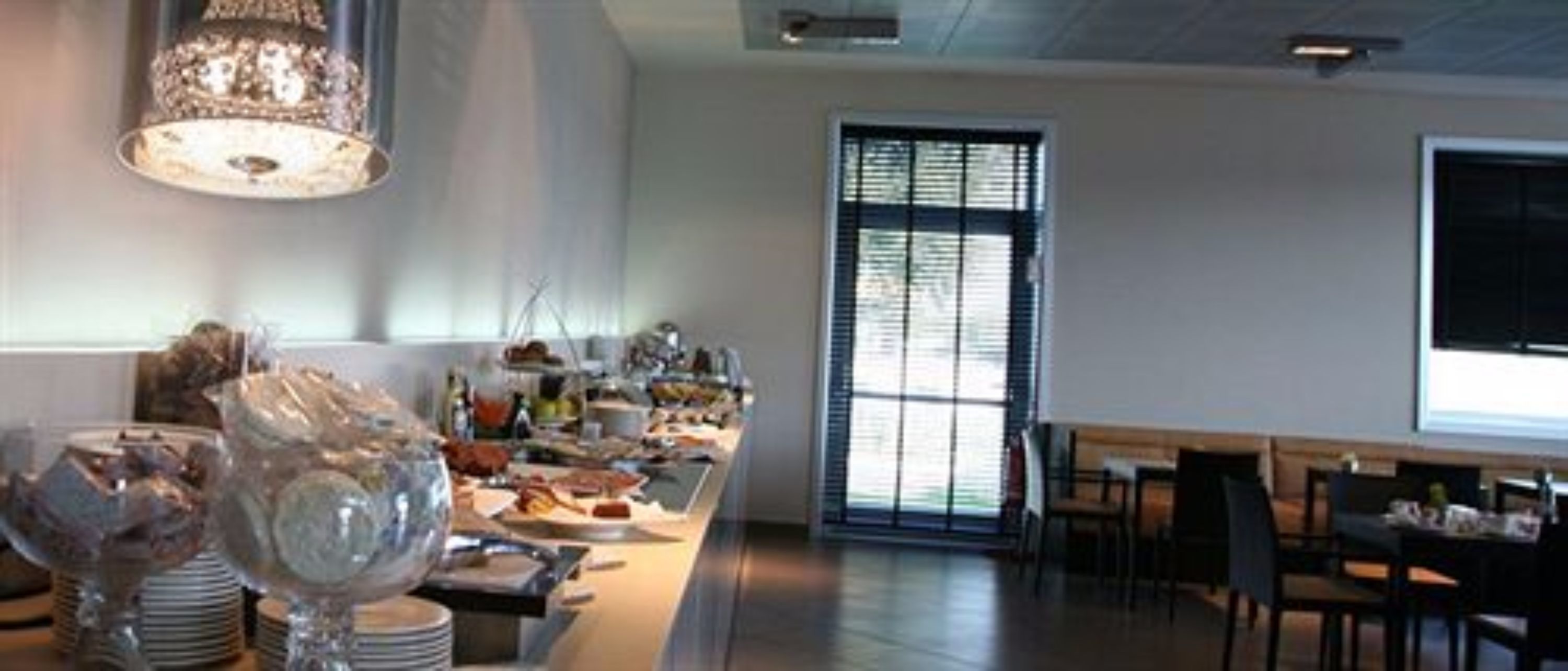 Un comedor moderno con una mesa larga, sillas y un amplio ventanal con persianas.