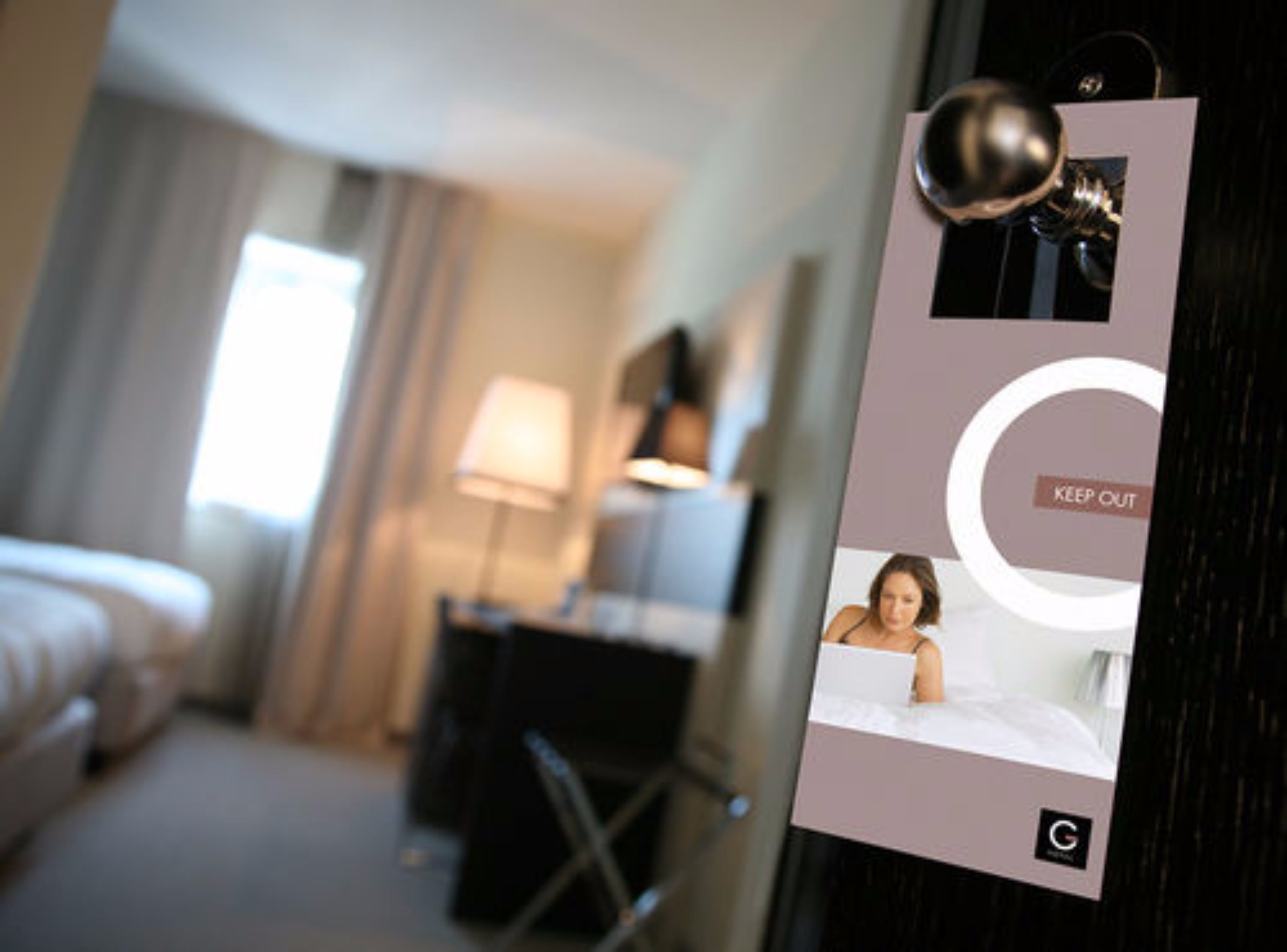 Habitació d'hotel amb un llit, un escriptori i una làmpada. Hi ha un senyal amb la inscripció "KEEP OUT".