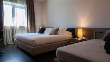 A hotel room with two beds, a bedside table with a lamp, and a window with curtains.