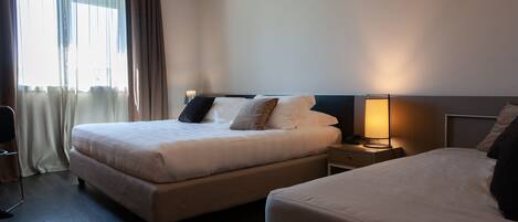A hotel room with two beds, a bedside table with a lamp, and a window with curtains.