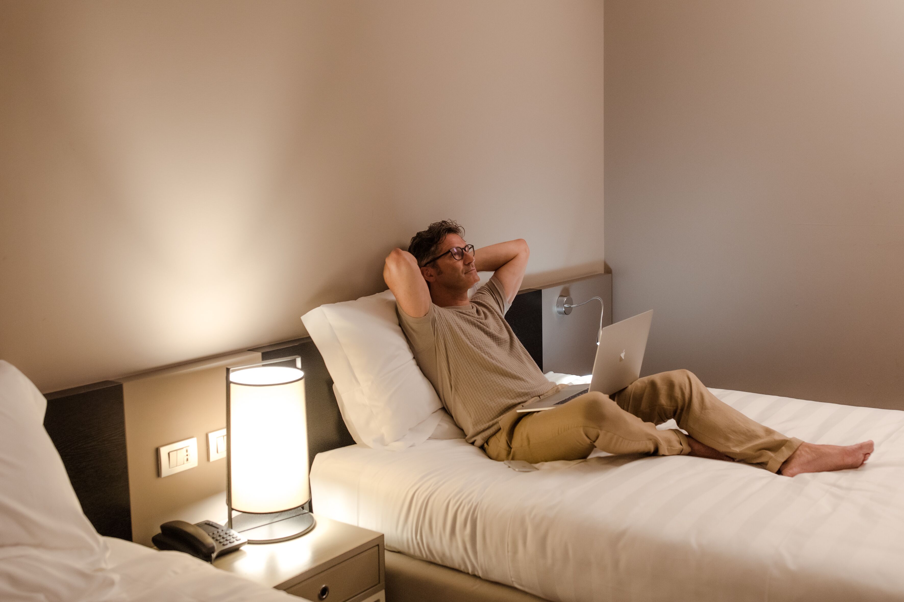 Quarto de hotel com uma cama, abajur, telefone e laptop na mesa de cabeceira.